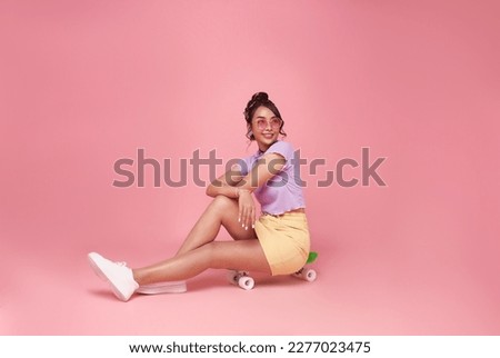 Full length of cheerful young asian teen woman sitting on skateboard have fun isolated on pink background studio portrait. People lifestyle concept. 