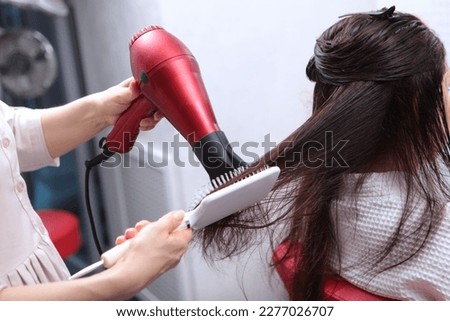 Long hair is styled with a hair dryer. A woman in a beauty salon. Long dark hair.Brush close-up. The concept of beauty salons. Royalty-Free Stock Photo #2277026707