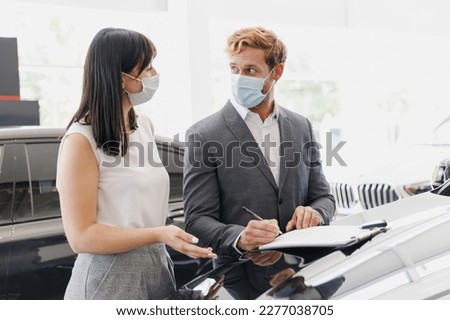 Man customer client buyer in suit pandemic mask choose auto want buy new car automobile consult with salesman sign documents on hood in showroom salon dealership store motor show indoor Sale concept