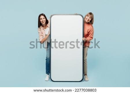 Full body elder parent mom with young adult daughter two women together in casual clothes big huge blank screen area mobile cell phone look camera isolated on plain blue background Family day concept Royalty-Free Stock Photo #2277038803