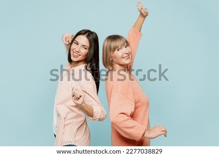 Side view smiling elder parent mom with young adult daughter two women together wearing casual clothes stand back to back dancing have fun isolated on plain blue cyan background. Family day concept