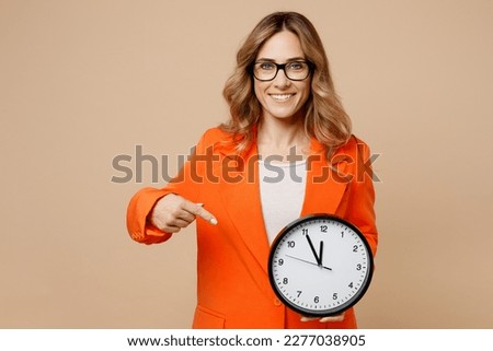 Young fun successful employee business woman corporate lawyer 30s wear classic formal orange suit glasses work in office hold in hands point finger on clock isolated on plain beige background studio Royalty-Free Stock Photo #2277038905