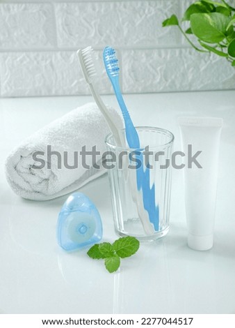 dental and mouth cleaning equipment consist of a toothbrush, toothpaste, mouth spray, dental floss, white towels. background of white bricks and green plants. concept simple product photography