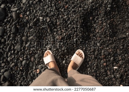 A picture of a woman's foot wearing pink sandals standing on the gravel stone of the seashore.