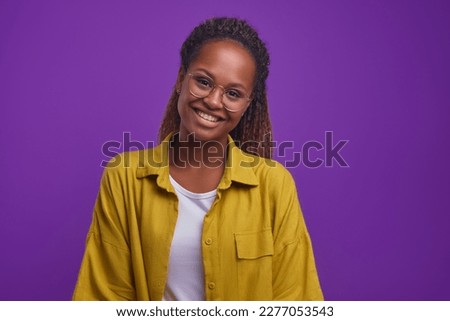 Young smiling attractive African American woman with long curly hair looks at camera wanting to share good mood and positive attitude to what is happening stands on isolated purple background