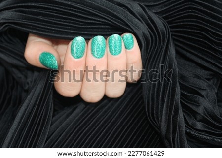 Woman's hand with green and silver manicure on a black background. Stylish fashionable woman's manicure. Nail polish. Artistic manicure. Modern style. Winter manicure.