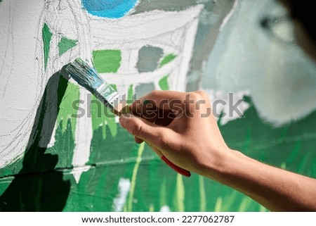 Girl artist hand holds paint brush and draws green nature landscape on white canvas at outdoor art painting festival, paintings art picture process. Woman artist paints atmospheric surreal picture Royalty-Free Stock Photo #2277062787