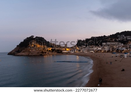 The sun sets over the golden sands of Tossa de Mar, Spain, casting a warm glow over the beach