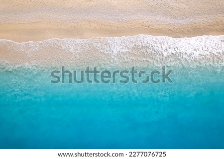 Aerial top down drone shot above an empty beach. The birds eye view of the amazing turquoise sea water and gentle waves crashing on an empty sand beach. Top down view over turquoise deep blue ocean