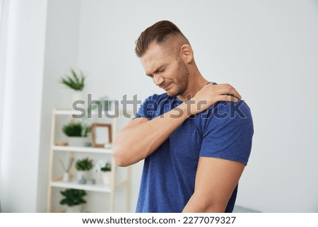 Man back neck and shoulder pain, inflammation of muscles and ligaments rupture during sports, inflammation and injury, in a blue t-shirt at home Royalty-Free Stock Photo #2277079327