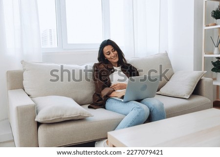 Woman freelancer on her day off sitting on the couch with a laptop at home and watching series and tv shows, smile