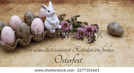 Easter egg with flowers and an Easter bunny figure in an egg box. German inscription means we wish our customers a happy Easter.
