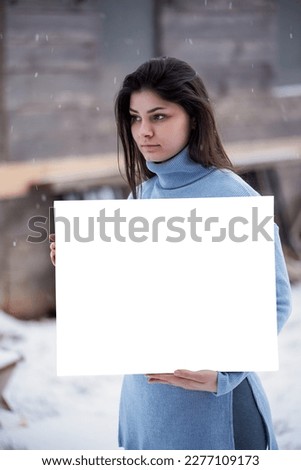 Beautiful woman holds a blank white card. Brunette girl while snow outdoors. Art mockup
