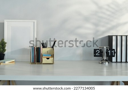 Creative workplace with blank picture frame, books and stationery on table with leaves shadow and sunlight