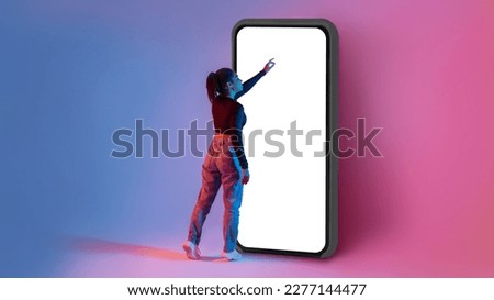 Full length shot of black lady touching screen of huge smartphone in colorful neon light, mockup for mobile app or website design. Woman interacting with big cellphone, space for ad Royalty-Free Stock Photo #2277144477