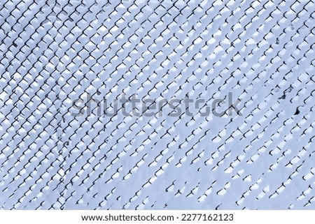 Icy net after the snow blizzard. Grey metallic diamond shaped background. Barbed wire after snow fall. White, blue, back texture. Frosty fence at snow day. 