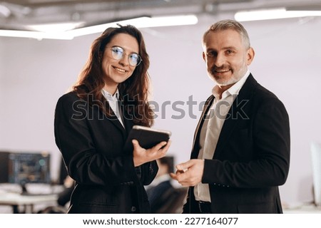 Smiling businessman and his personal assistant standing in office. Businesswoman with tablet posing with her boss. Happy business partners Royalty-Free Stock Photo #2277164077