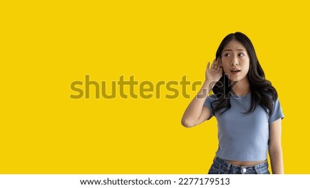 Asian woman eavesdropping or overhearing secret conversation isolated on yellow background, Gossip, Listening, Yellow background studio portrait.