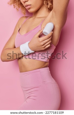 Cropped shot of unrecognizable woman applies deodorant under armpit protects skin from sweat wears cropped top and leggings has slim fit body isolated over pink background reduces body odor. Royalty-Free Stock Photo #2277181109