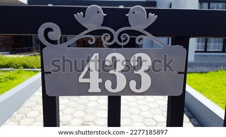 Number on gray plastic plate installed on the black metal gate
