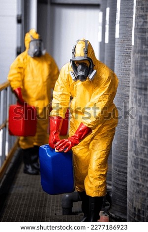Fully protected workers in yellow hazmat suit, gas masks and gloves handling dangerous chemicals or substances. Royalty-Free Stock Photo #2277186923