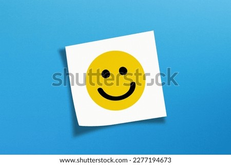 Happy smiley face emoticon with white note paper on blue background Royalty-Free Stock Photo #2277194673
