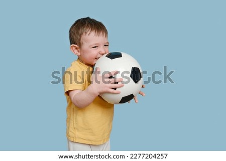 Happy toddler baby with a soccer ball on a studio blue background. Child boy holding a sports ball in his hands. Kid age one year eight months