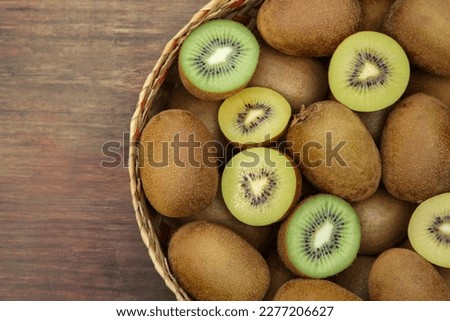 Basket of many whole and cut fresh kiwis on wooden table, top view