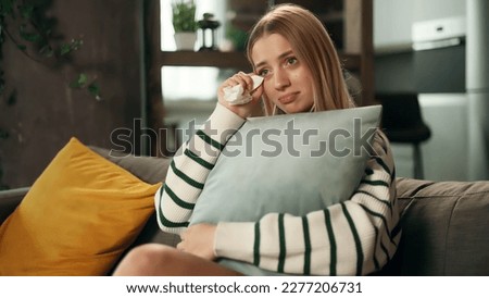 Portrait if sensitive young attractive woman sits on sofa at home alone hugging a pillow and watch drama film Beautiful blond girl wipes away tears after watching film Royalty-Free Stock Photo #2277206731
