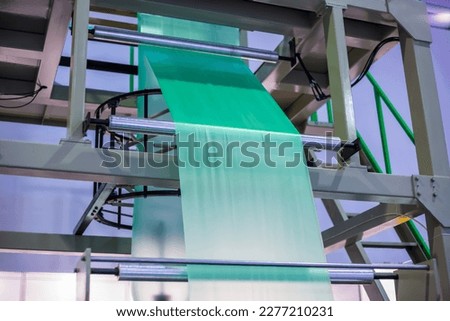 Part of automatic plastic bag making machine with flat polyethylene green film at exhibition, trade show. Manufacturing, recycling, industry and automated technology equipment concept Royalty-Free Stock Photo #2277210231