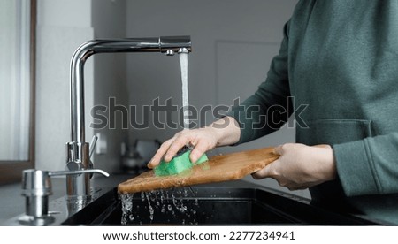 woman washing wooden cutting board under water stream in sink in the kitchen, cleaning at home, no face Royalty-Free Stock Photo #2277234941