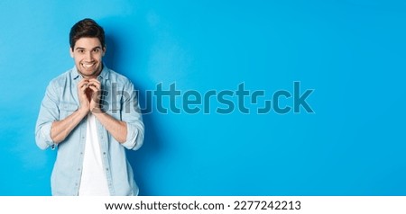 Funny cunning man having evil plan, scheming something and smiling devious, standing against blue background.