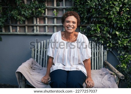 Happy mature woman on a bench. Smiling woman with short hair relaxing in backyard. Royalty-Free Stock Photo #2277257037