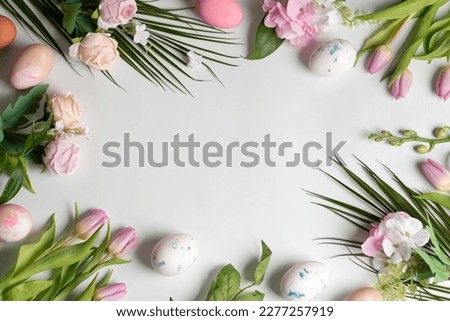 Easter card with spring rose and tulip flowers and painted Easter eggs top view flat lay on white background