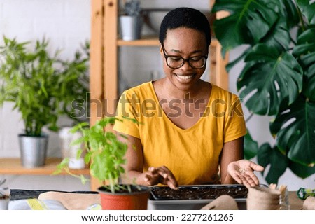 Young smiling african-american woman doing seed-starting early in the spring indoors for her backyard garden or a homestead garden Royalty-Free Stock Photo #2277261265