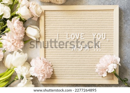Happy Mother's Day. Letter I LOVE MOM on letterboard and beautiful spring flowers on light background. Womans day, wedding, mothers day greeting card. View from above. 