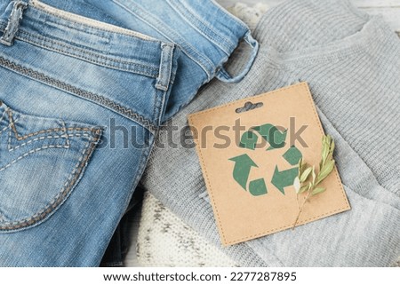 Sustainable still life with Blue denim jeans, gray pullover and craft paper card with Recycling symbol. Second hand apparel idea. Circular fashion, donation, charity concept. Top view