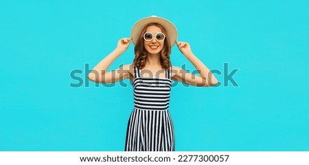 Summer portrait of beautiful young woman wearing straw round hat, striped dress on blue background