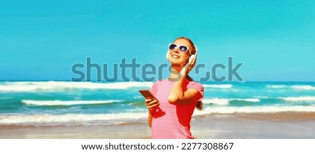 Summer portrait of fitness happy woman with smartphone listening to music in headphones on the beach on sea background