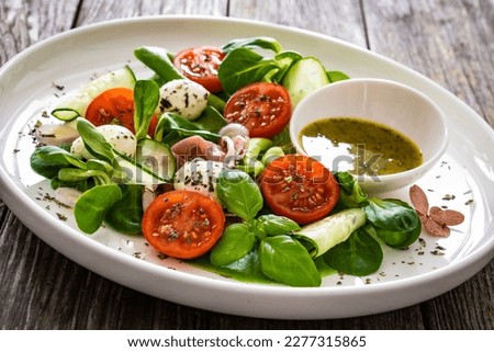 Fresh salad - prosciutto di Parma, mozzarella, cucumber, tomatoes and leafy vegetables on wooden table  Royalty-Free Stock Photo #2277315865