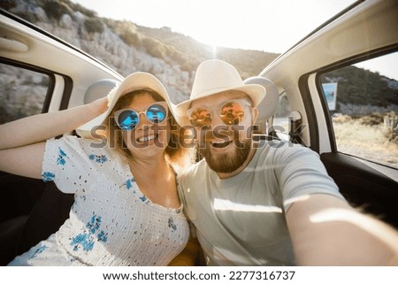 Romantic couple making selfie on smartphone camera in rental cabrio car on ocean or sea beach enjoying summer vacation together and taking picture on cellular resting near sea on weekends