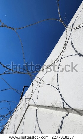 Barbed wire on white wall and blue sky. Abstractnaf photo with symmetry and shadows. High quality photo