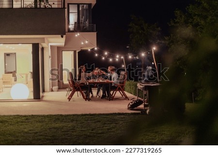 A group of young diverse people having dinner on the terrace of a modern house in the evening. Fun for friends and family. Celebration of holidays, weddings with barbecue. Royalty-Free Stock Photo #2277319265
