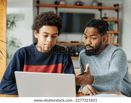 Father and son doing homework with laptop at home. Father and teenage son using laptop. Boy and dad sitting at home working with notebook Royalty-Free Stock Photo #2277321831