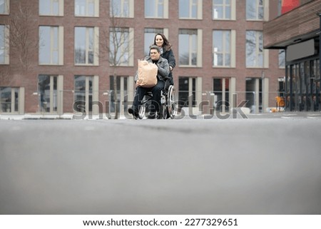a woman pushes a physically disabled person in a wheelchair after shopping