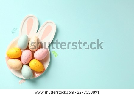 Bunny shaped plate with colorful Easter eggs on blue background. Happy Easter greeting card design.