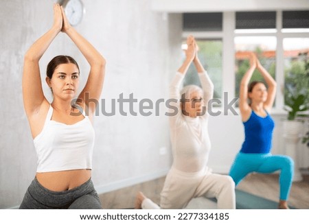 Motivated fit sports women balancing in Virabhadrasana 1 or warrior 1 pose on mats for strengthing during yoga class together