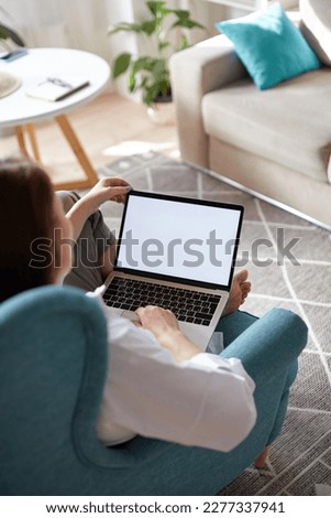 Mockup white screen laptop woman using computer sitting on armchair at home, back view, focus on screen