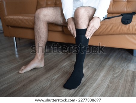 A man in a white shirt putting on black medical compression socks. Dressing up.