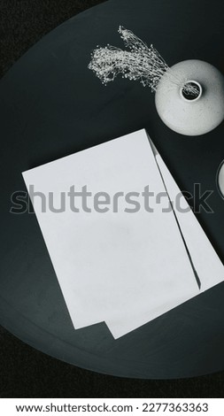 two pieces of paper or books with plain white covers piled on a table with a pot as decoration